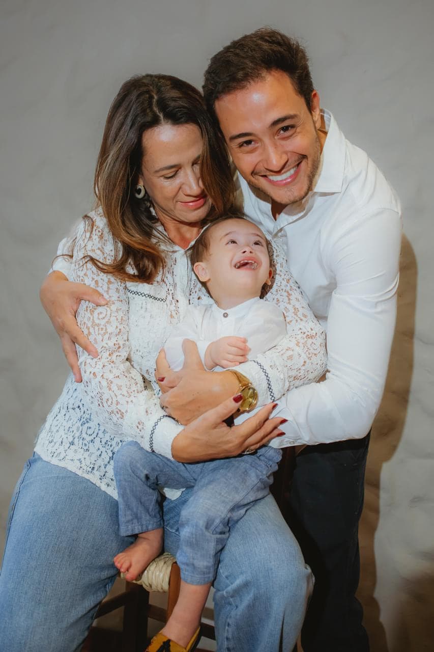 Marcos Vinicius Flores Piva com a esposa e o filho no colo, os três sorrindo